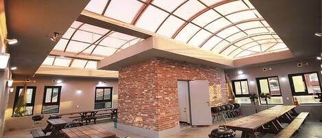 Amplio espacio interior con techo alto y tragaluces, que cuenta con varias mesas de picnic y una estructura de ladrillo.