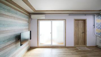 Una habitación con piso de madera, un televisor de pantalla plana montado en la pared, una puerta corrediza de vidrio y un salpicadero de azulejos en la zona de la cocina.
