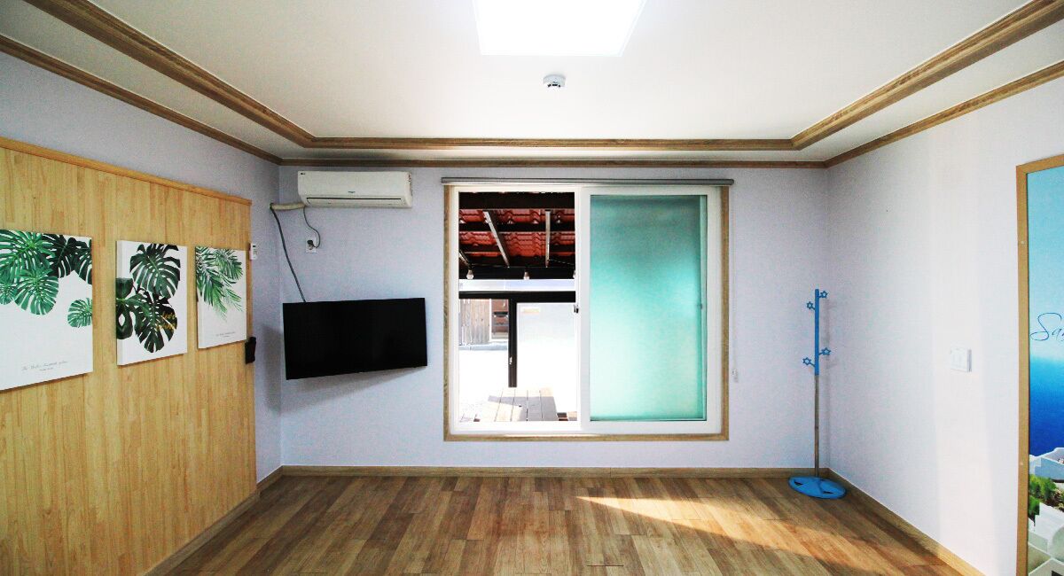 A room with wooden flooring, a mounted TV, a sliding glass door, and a blue floor lamp.