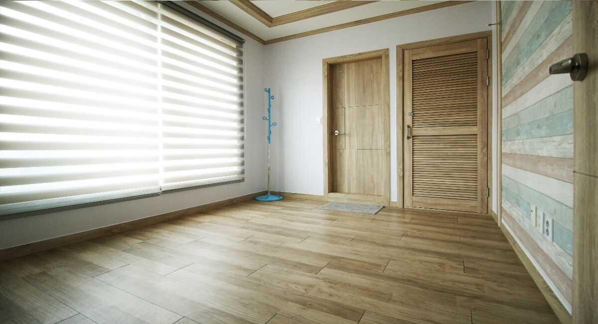 A room with wooden flooring, a large window with blinds, two wooden doors, and a blue floor lamp.