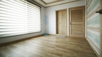 A room with wooden flooring, a large window with blinds, two wooden doors, and a blue floor lamp.