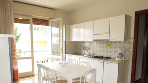 A kitchen with white cabinets, a gas stove, a coffee maker, and a dining table with four chairs. - Nice apartment for 5 guests with A/C, TV, balcony and pets allowed (Ca Grande Pineda)