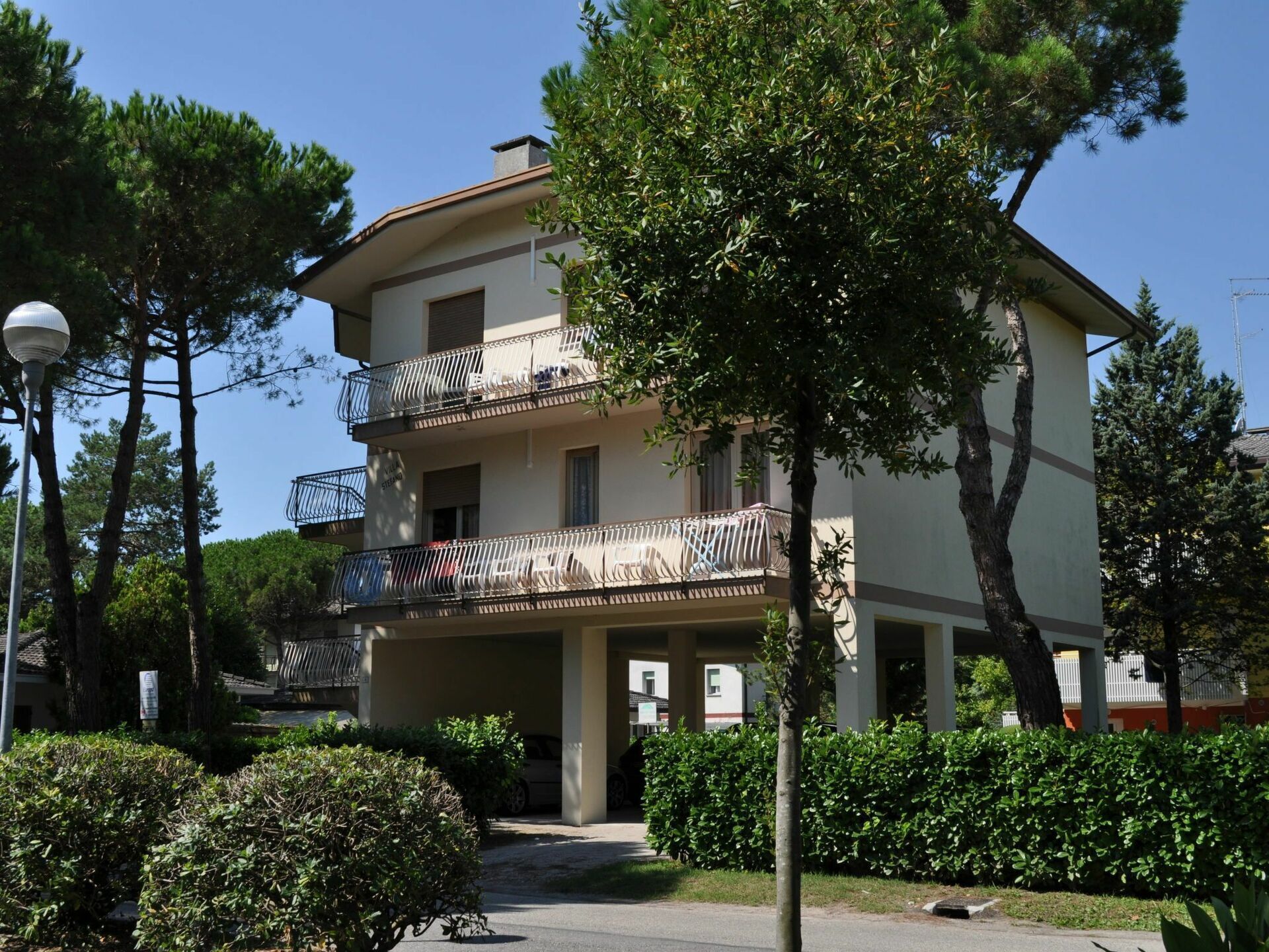 A multi-story building with balconies, surrounded by trees and greenery.