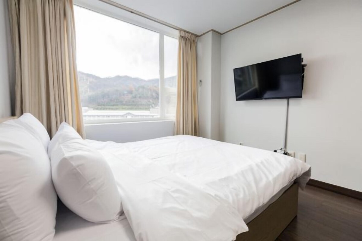 A hotel room with a bed, a TV mounted on the wall, and a window with curtains.