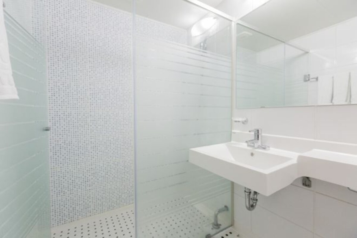 A modern bathroom with a glass shower enclosure, a white sink, and a large mirror.