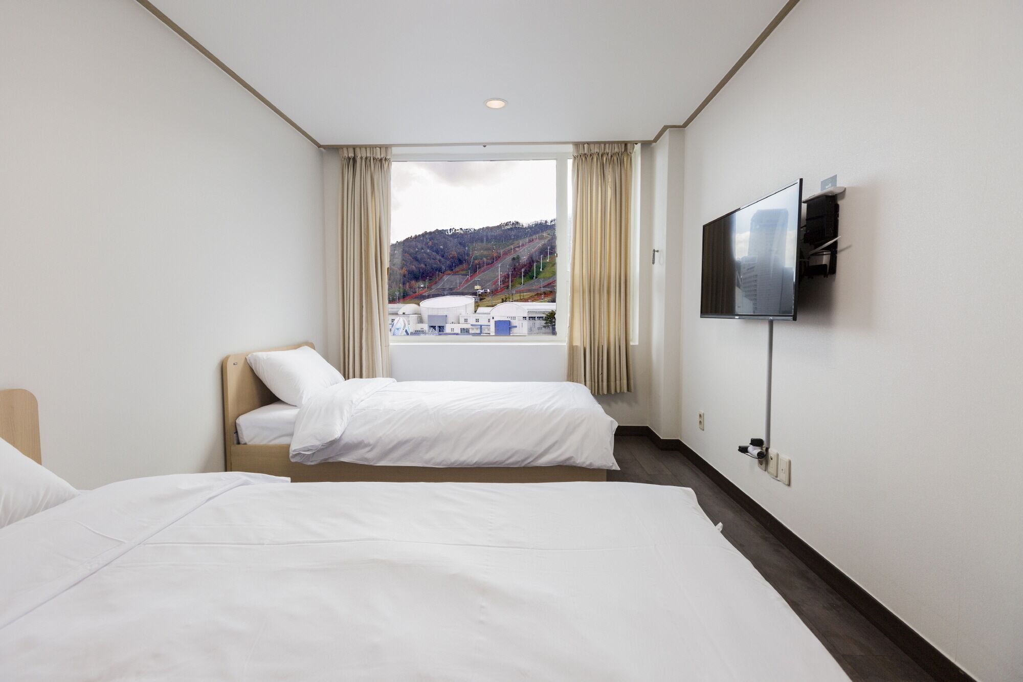 Quarto de hotel com duas camas, televisão e janela com vista para uma paisagem montanhosa.