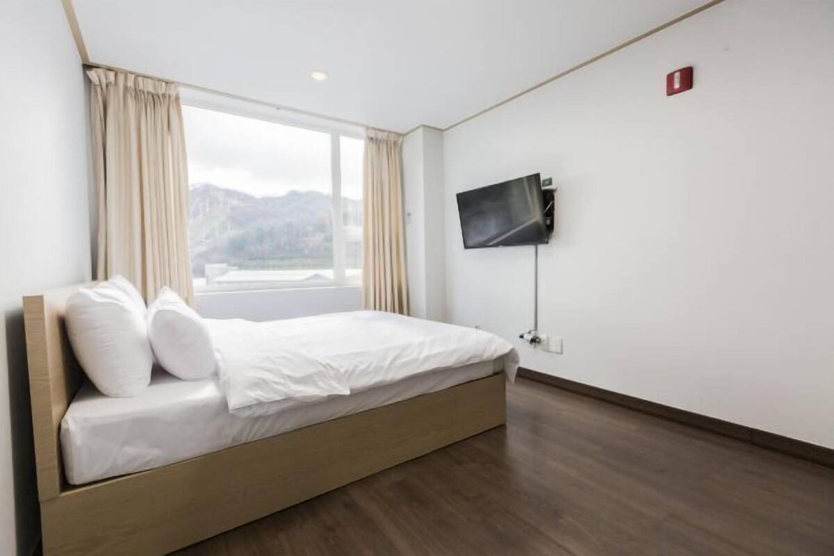 A hotel room with a bed, a TV, and a window with curtains.