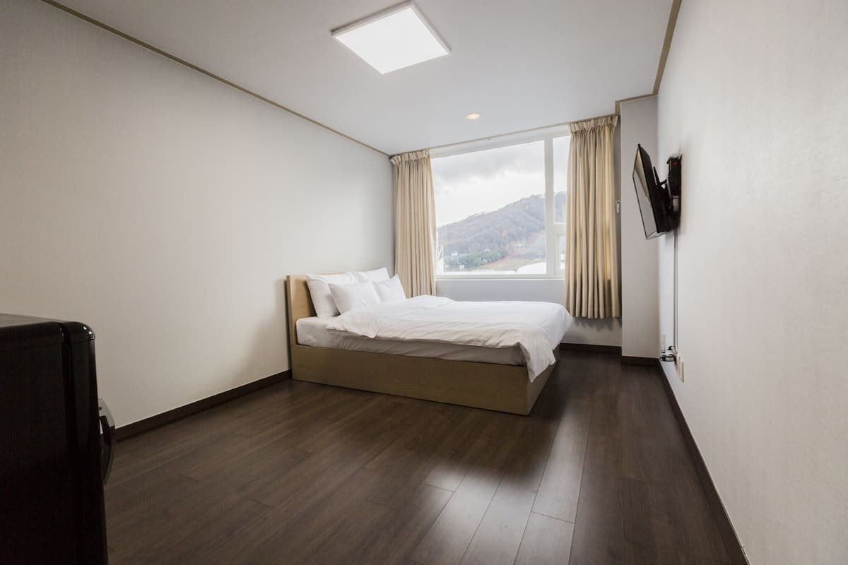 A bedroom with a bed, a TV mounted on the wall, and a window with curtains.