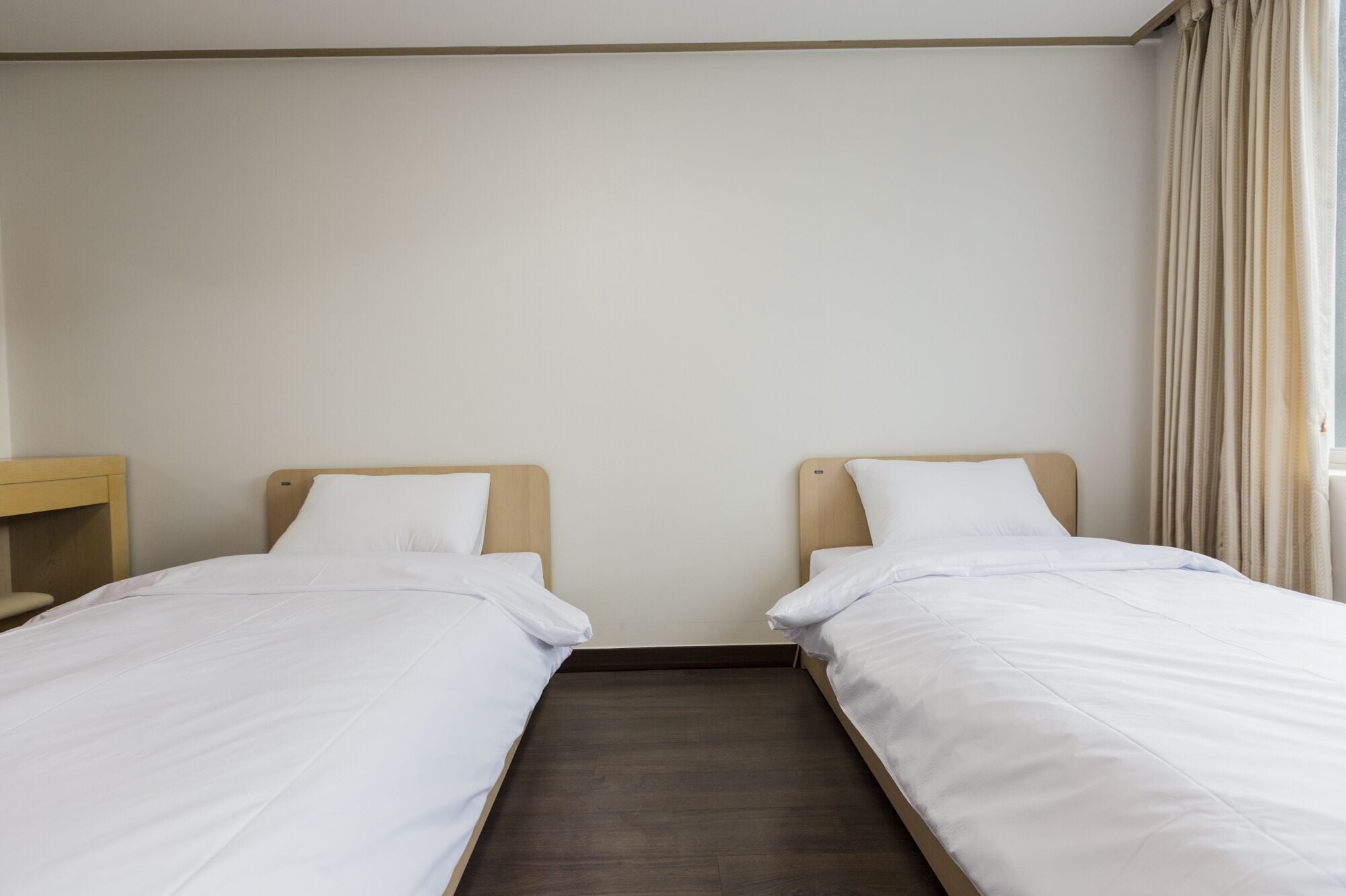 A twin room with two single beds, a wooden headboard, a nightstand, and a window with curtains.
