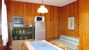 Una cocina compacta con paredes de madera, una mesa de comedor con sillas, un microondas, un refrigerador y un televisor.