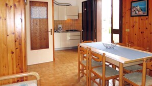 Una habitación revestida de madera con paneles, una mesa de comedor y sillas, una zona de cocina con armarios y una estufa, y una puerta con un panel de vidrio esmerilado.
