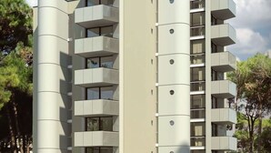 Un immeuble résidentiel moderne à plusieurs étages, doté de balcons, d’un toit plat et entouré d’un espace paysager aménagé.