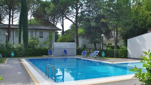 A rectangular swimming pool with a tiled deck, surrounded by trees and a building with a tiled roof. - Beautiful  villa for 6 guests with pool, A/C, TV, terrace and pets allowed (San Michele Al Tagliamento)