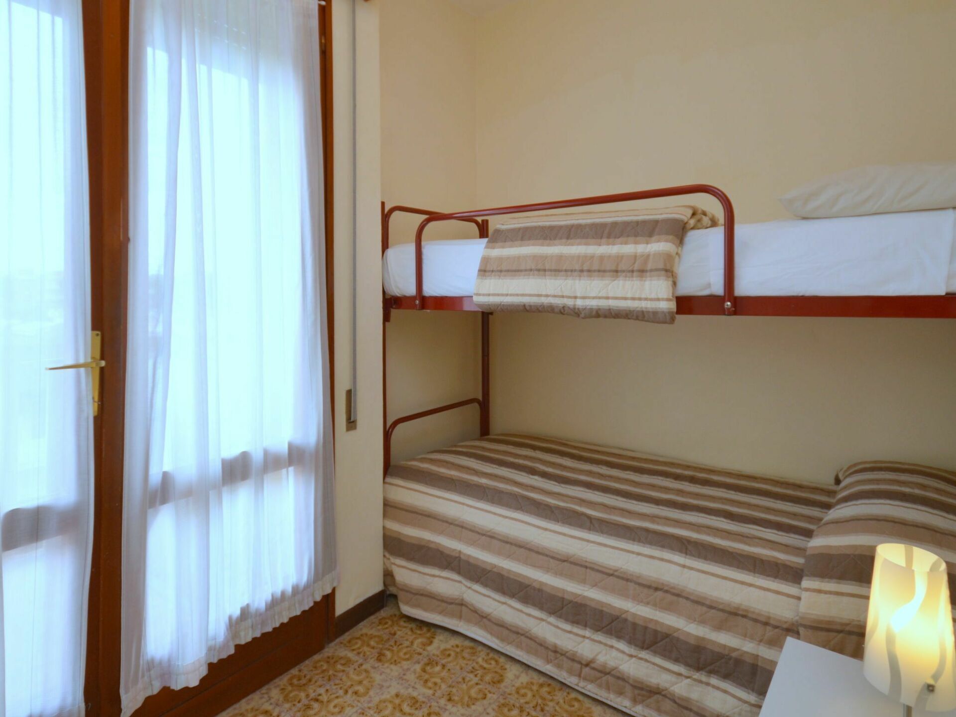 Una habitación con una cama litera, una puerta con cortina y una lámpara sobre una mesita.