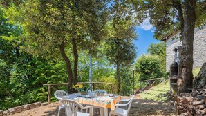 An outdoor dining area with a table and chairs, surrounded by trees and a stone building. - Stunning private villa for 4 guests (Pontestazzemese)