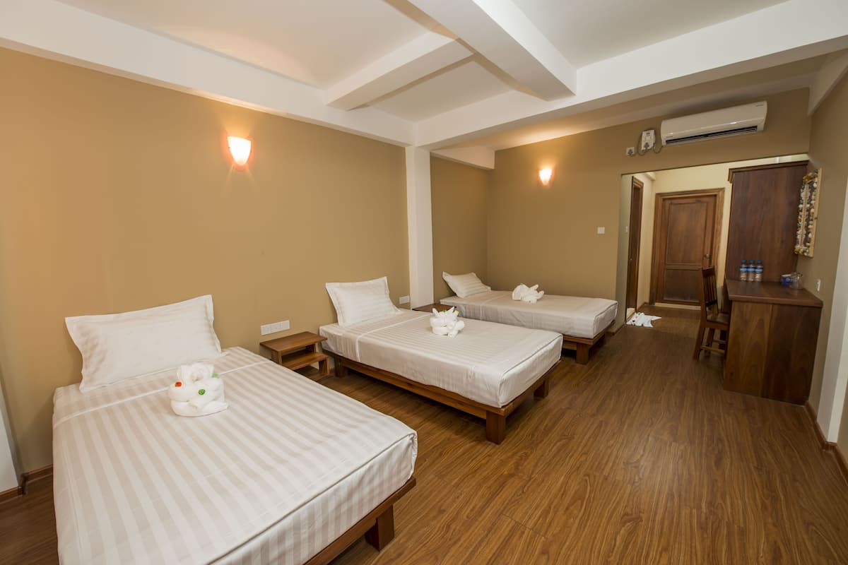 A hotel room with three single beds, wooden flooring, and a small desk with a chair.
