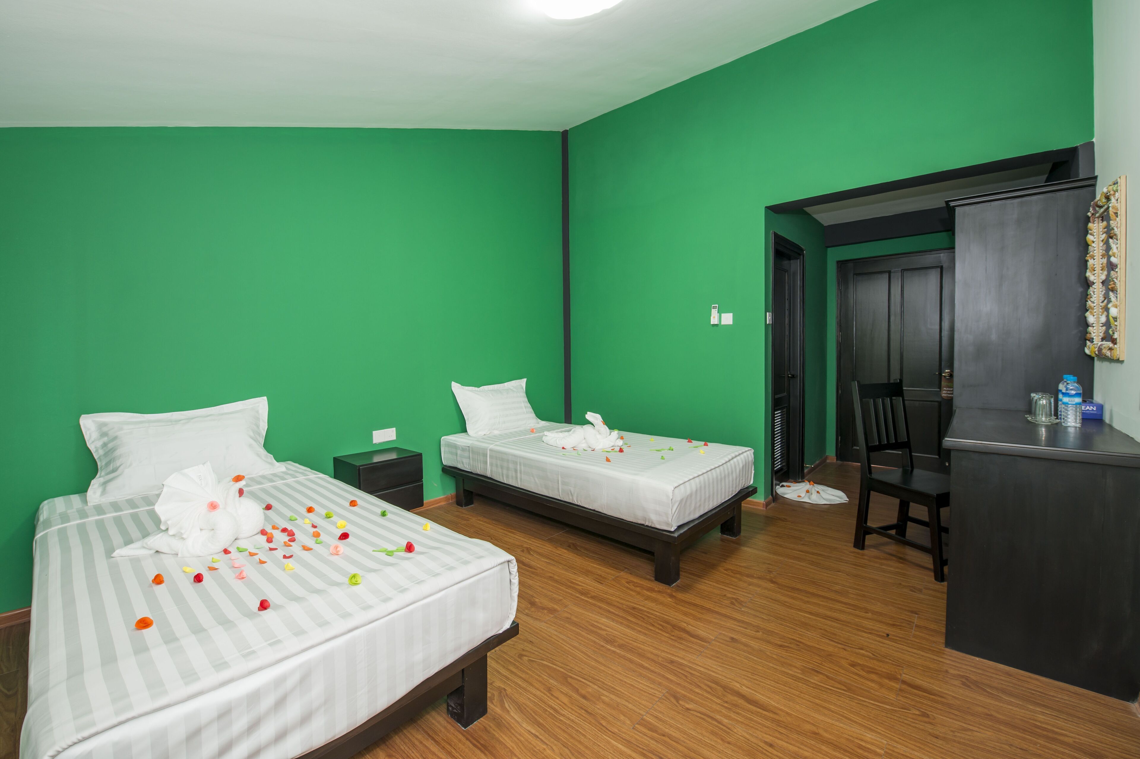 Una habitación de hotel con dos camas, paredes verdes, suelo de madera, un escritorio y una silla.