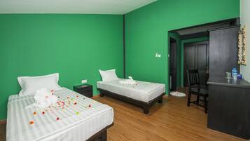 Una habitación de hotel con dos camas, paredes verdes, suelo de madera, un escritorio y una silla.