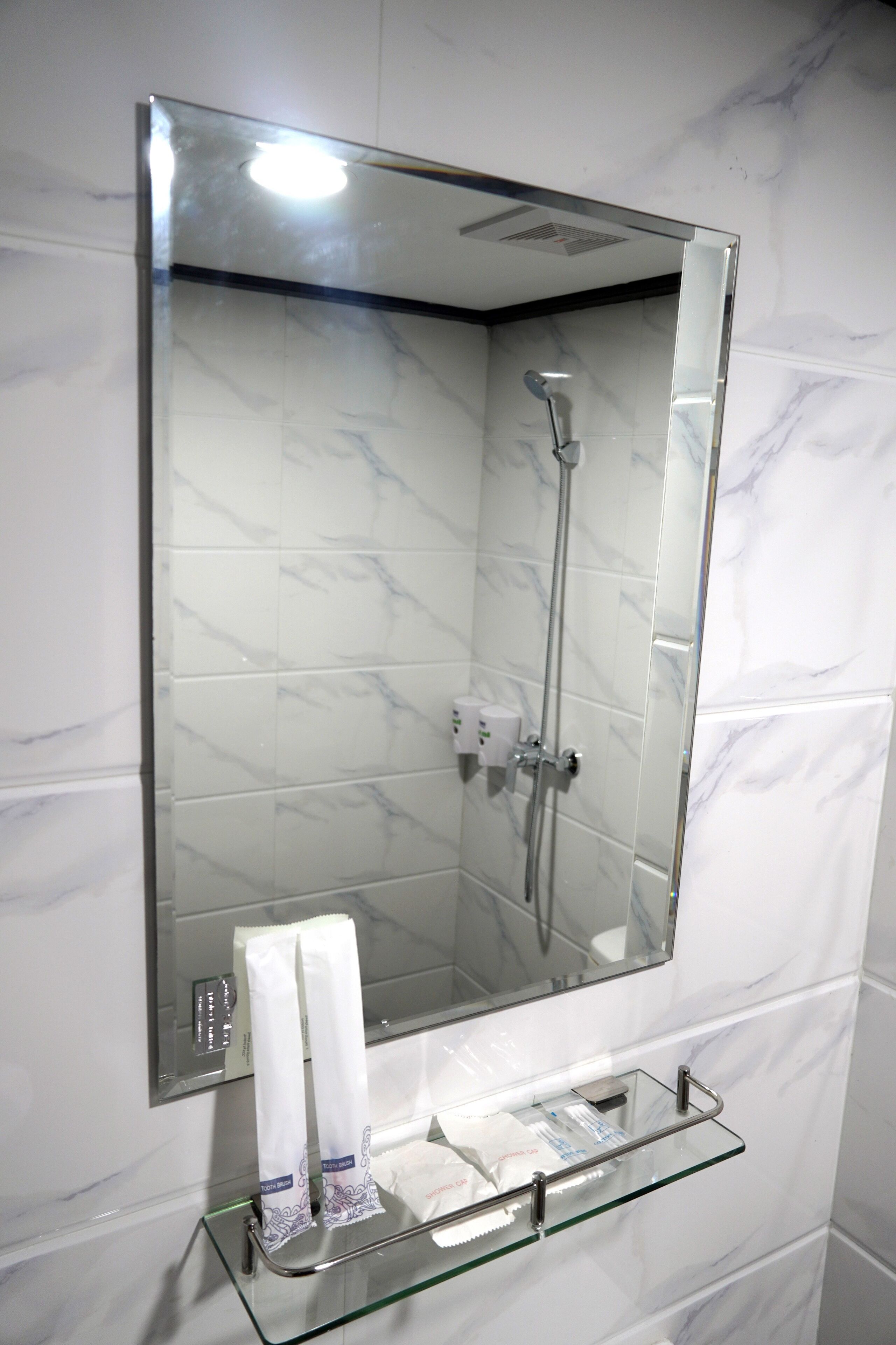 Un baño con repisas de vidrio para artículos de aseo, un espejo sobre el lavabo y una ducha con cabezal de ducha manual.