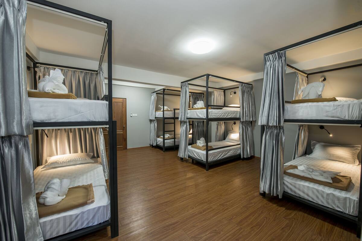 A dormitory room with four bunk beds, each with a canopy, and a wooden floor.