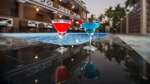 Two cocktails on a reflective surface near a poolside area with a building in the background. - Traveller Lodge Ngapali by River Top - Hostel (Ngapali)