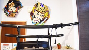 A display of traditional Japanese swords on a wooden stand in a room with a wooden door and a small potted plant. - Start One Home Senzoku A (Tokyo)