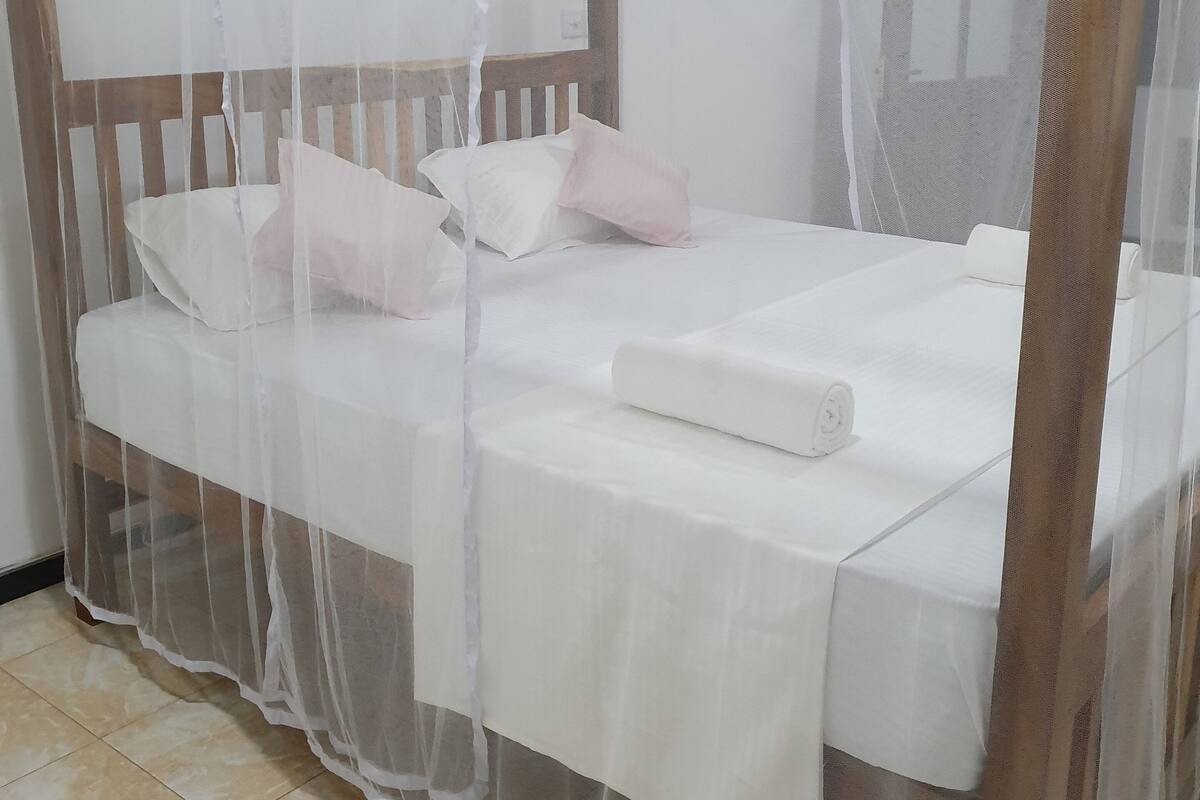 A four-poster bed with a canopy, white bedding, and two pillows.