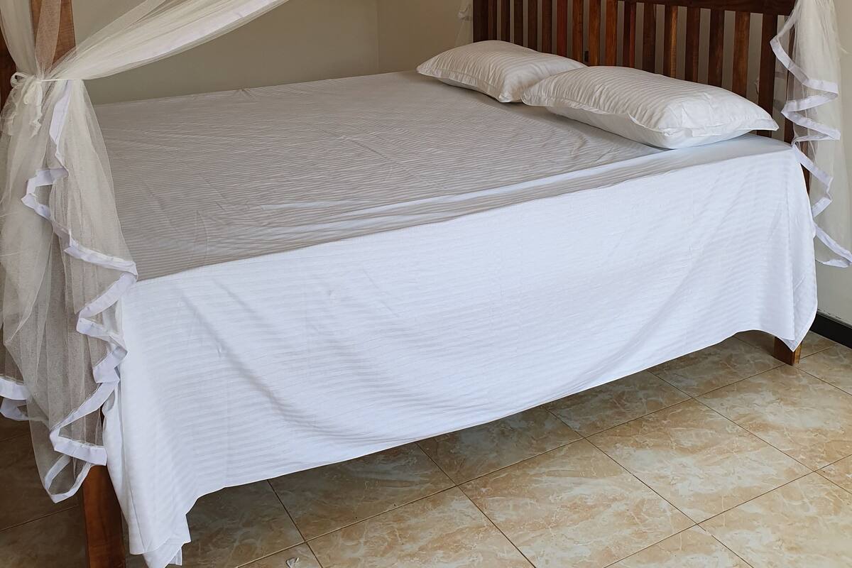 A four-poster canopy bed with white linens and a wooden frame.