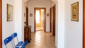 A hallway with a tiled floor, a wooden door at the end, and blue chairs on the left.