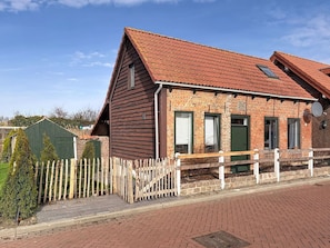 A brick building with a sloped roof, a wooden fence, and a paved walkway.