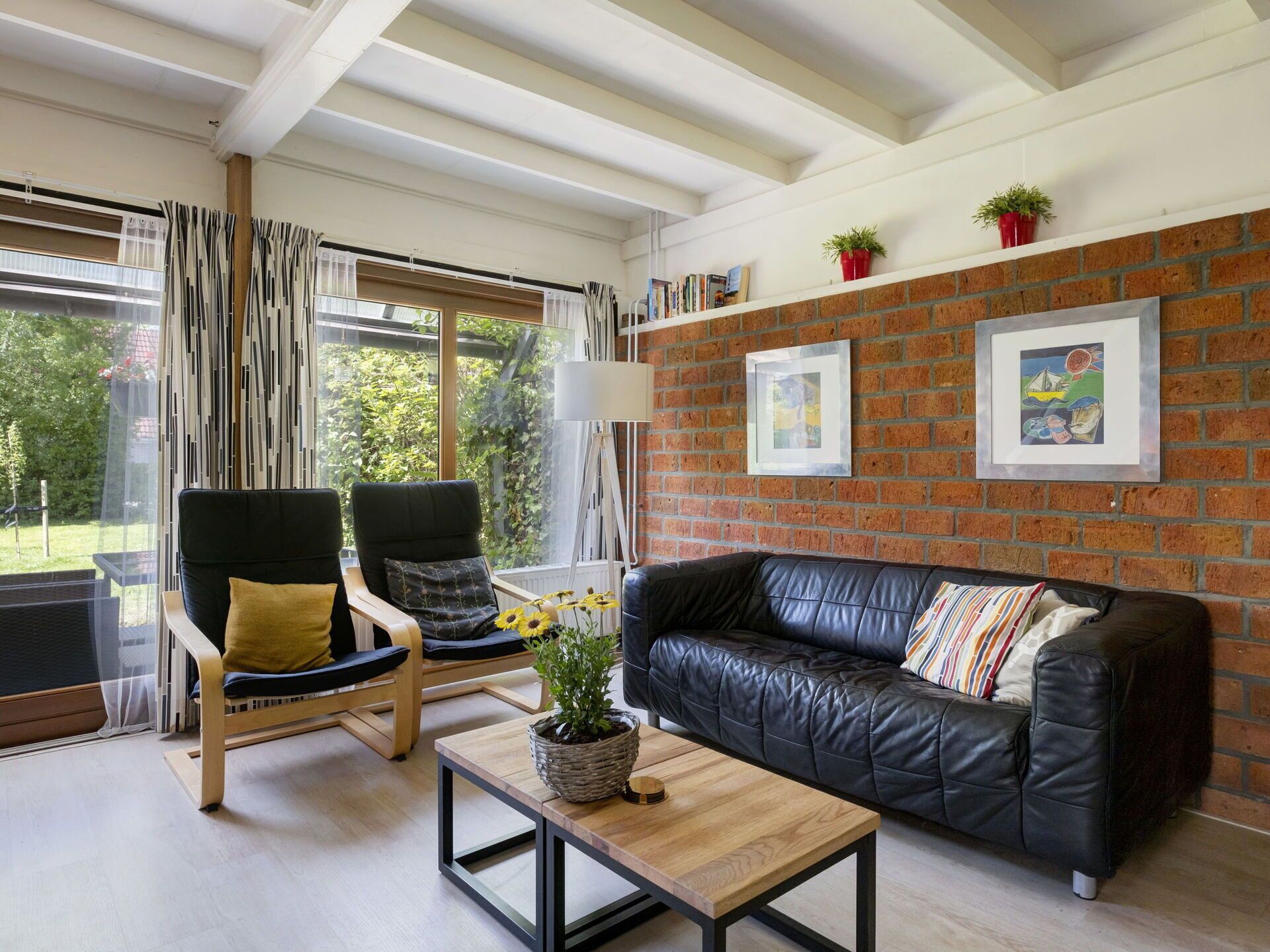 Una sala de estar moderna con un sofá de cuero negro, dos sillones, una mesa de centro de madera y una pared de ladrillo con obras de arte enmarcadas.