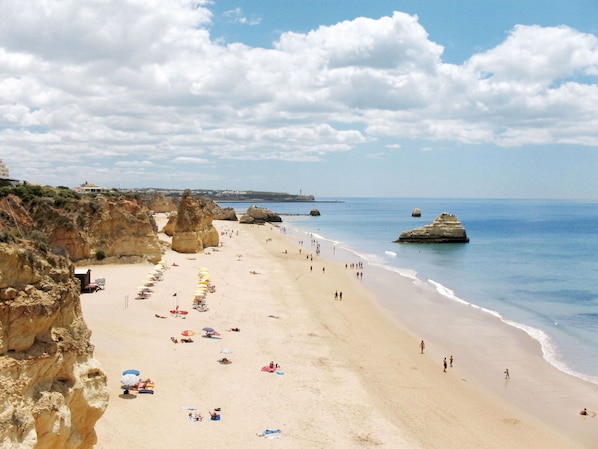 Enjoy the serene beach scene with a wide sandy shore, beach umbrellas, and stunning rock formations.