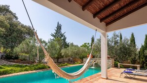 A pool with a hammock, surrounded by greenery and stone walls.