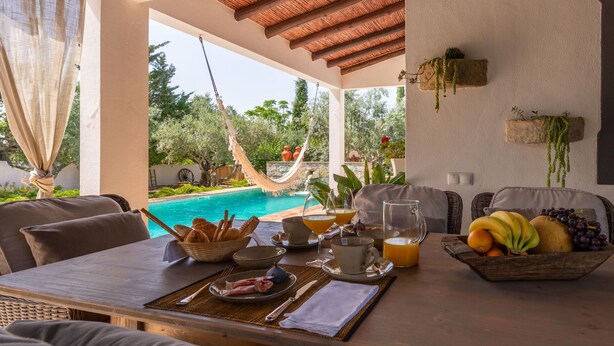 A dining area with a pool view, outdoor seating, and a hammock.