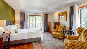 A bedroom with a bed, a desk, two chairs, a dresser, and a window with curtains.