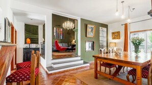 A spacious living area with a dining table, red chairs, a chandelier, and a staircase leading to another room.