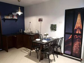 A dining area with a table set for four, a kitchen area with a sink and a kettle, and a large window with a cityscape view. - Aurora Court (George Town)