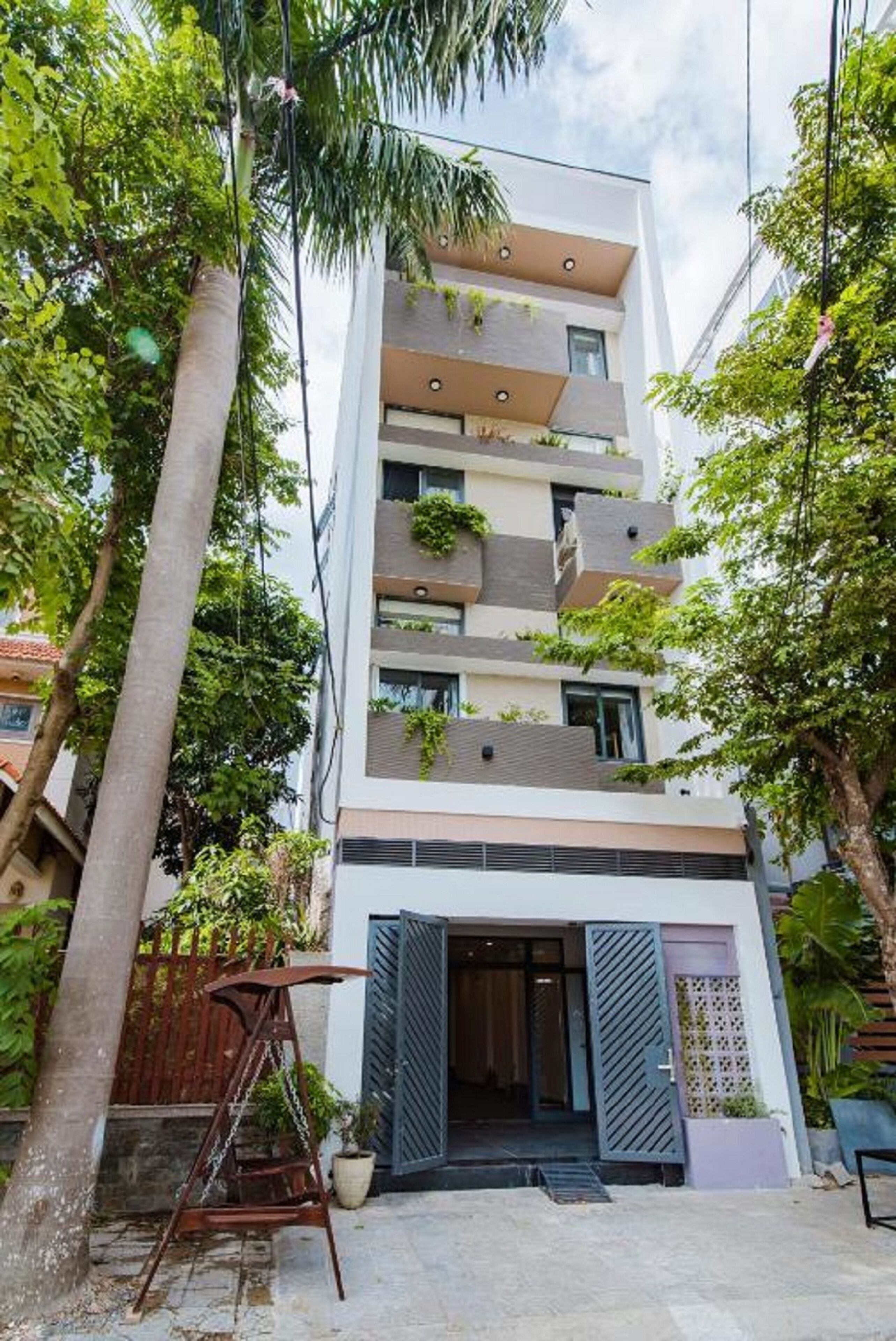 A modern multi-story building with balconies, a gated entrance, and surrounding greenery.
