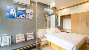 A modern bedroom with a bed, a bedside table, a built-in bench, and a wardrobe. There are wall-mounted air conditioning units and framed artwork depicting coastal scenes. - The Art - An Homestay (Da Nang)