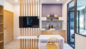 A modern kitchen with a flat-screen TV, wooden cabinets, and a dining area with a bench and chairs. - The Art - An Homestay (Da Nang)