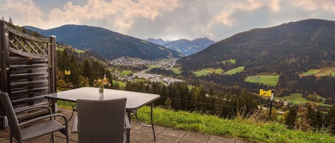 A patio with a table and chairs overlooking a valley with mountains.