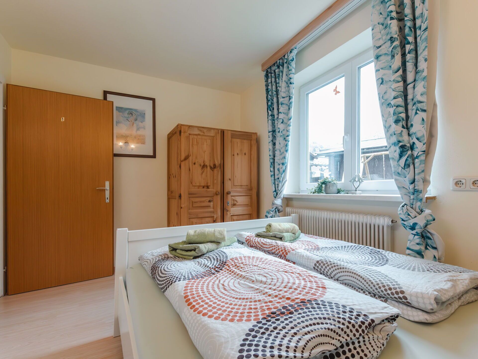 Quarto com cama, guarda-roupa, janela com cortinas e radiador.