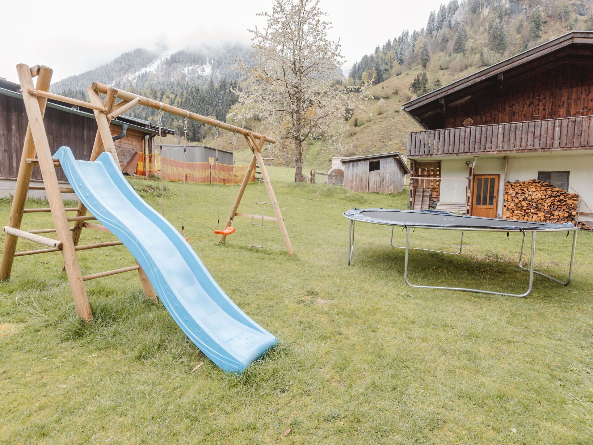A playground with a slide and swings, a trampoline, and a building with a wooden exterior.