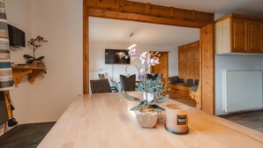 A modern kitchen with wooden cabinets, a dining table with a vase of flowers, and a television mounted on the wall. - Beautiful  villa for 16 guests with WIFI, TV and terrace (Piesendorf)