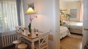 Una habitación con una mesa de comedor de madera, sillas, una lámpara y una cama con colcha blanca.