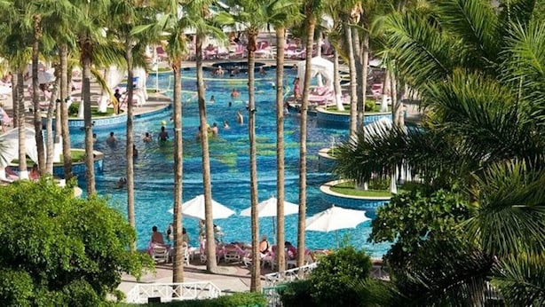 Un área de piscina en un resort, con varias piscinas rodeadas de palmeras y sillas de descanso.