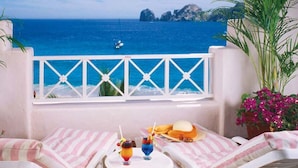 Un balcón con vista al mar, una mesa con bebidas y comida, y cojines a rayas.