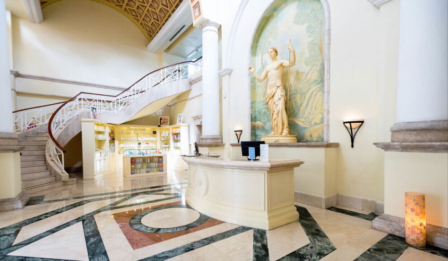 A lobby with a marble floor, a reception desk, a staircase, and a large mural.