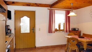 A kitchen with a wooden door, a dining table with chairs, a red rug, and a ceiling fan.