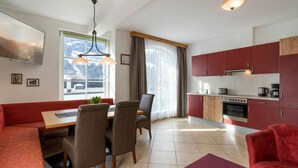 Een moderne keuken met rode kastjes, een eethoek met een houten tafel en stoelen, en een groot raam met uitzicht op een besneeuwd landschap.